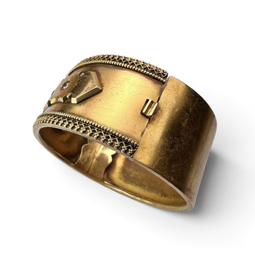 fig 1. A wide Victorian Etruscan Revival gold hinged bangle decorated with intricate beadwork borders and star-set gemstones across a central band.