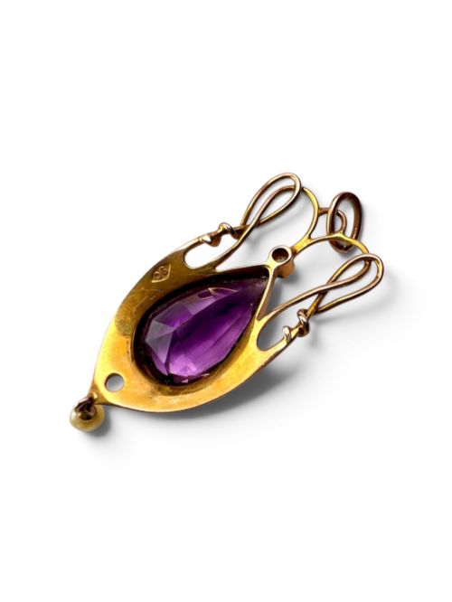 fig 1. An Art Nouveau gold pendant features an openwork whiplash frame surrounding a central pear-cut purple amethyst gemstone, anchored by a small pearl above and a dangling seed pearl below.