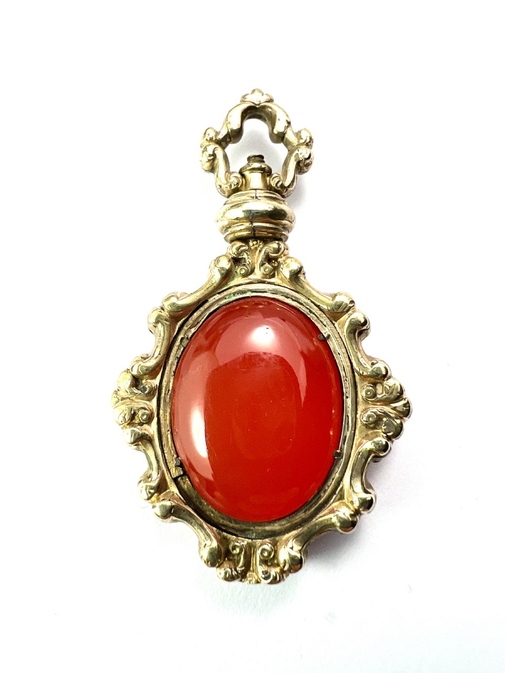 An ornate Georgian gilt metal swivel fob pendant featuring a polished oval red carnelian stone set within a scrollwork frame. View II