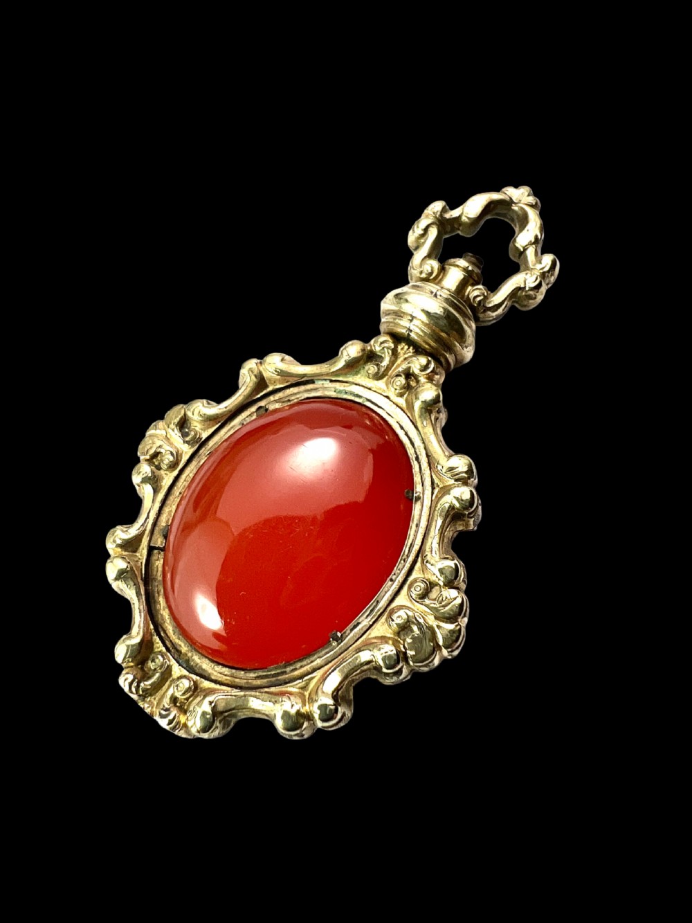An ornate Georgian gilt metal swivel fob pendant featuring a polished oval red carnelian stone set within a scrollwork frame. View III