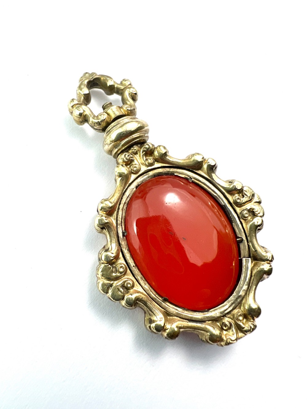 An ornate Georgian gilt metal swivel fob pendant featuring a polished oval red carnelian stone set within a scrollwork frame. View V