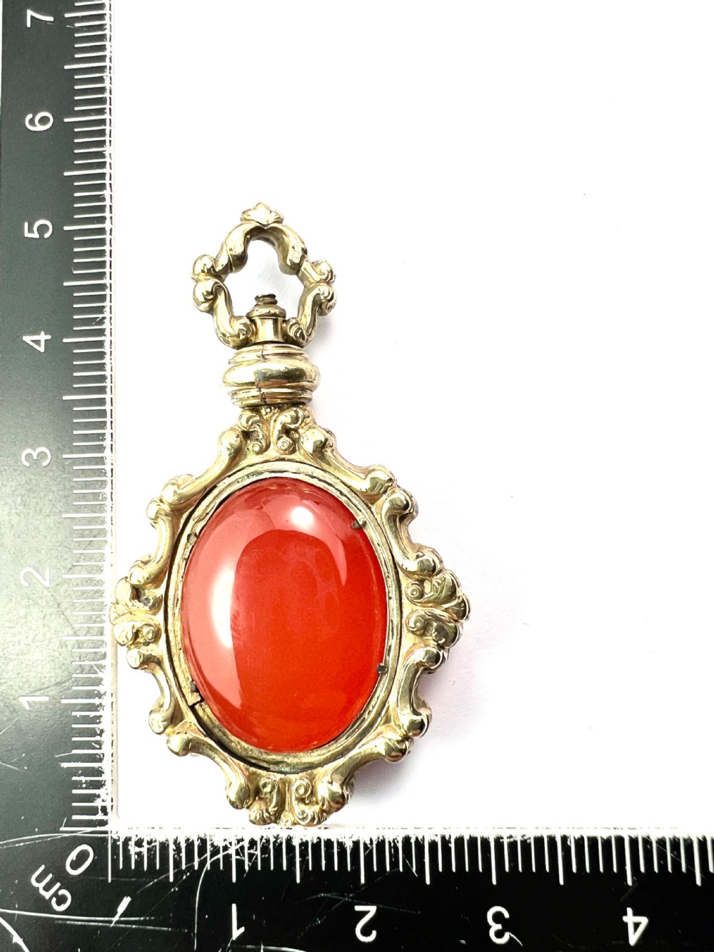 An ornate Georgian gilt metal swivel fob pendant featuring a polished oval red carnelian stone set within a scrollwork frame. View VI