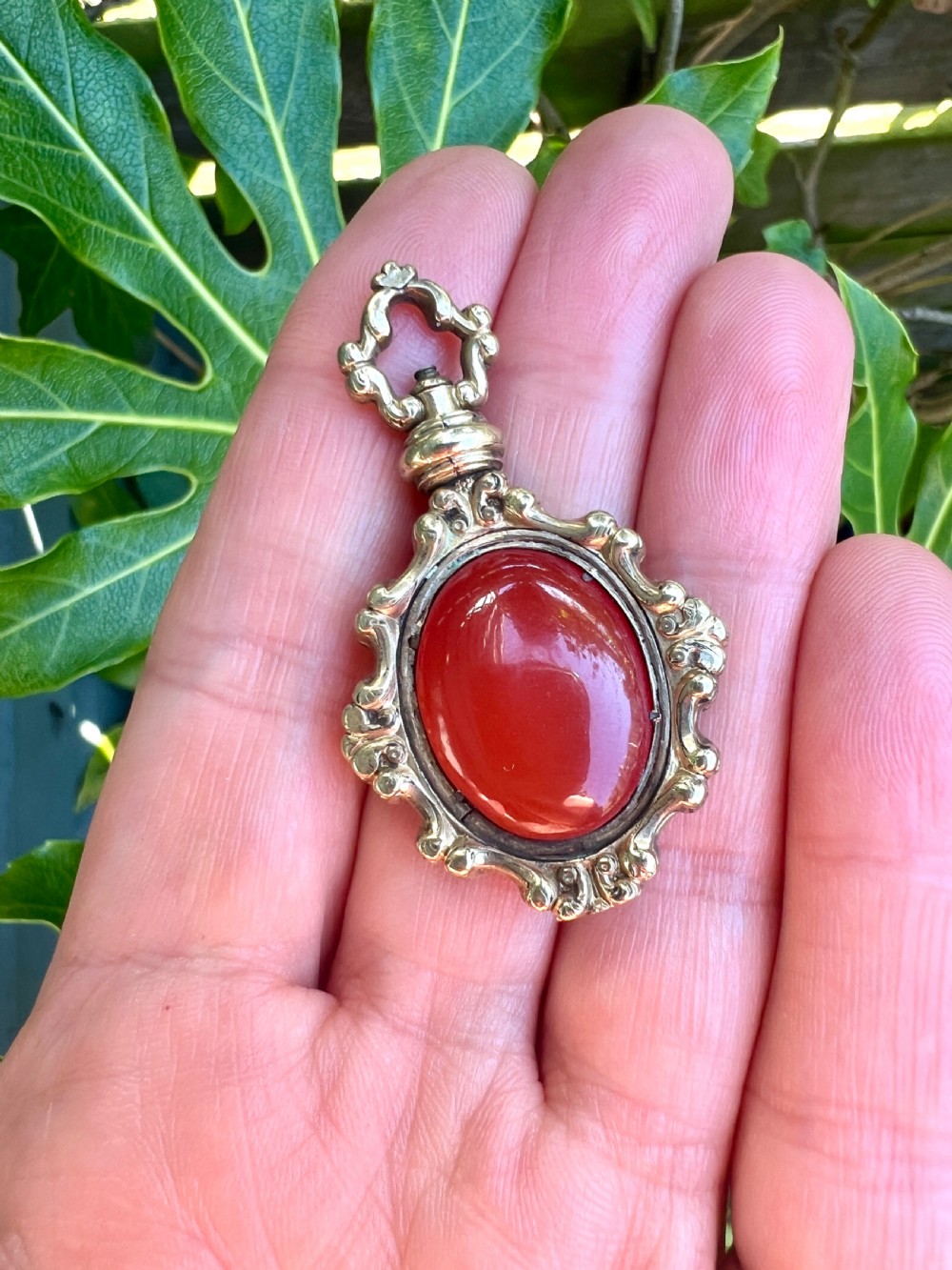 An ornate Georgian gilt metal swivel fob pendant featuring a polished oval red carnelian stone set within a scrollwork frame. View VII