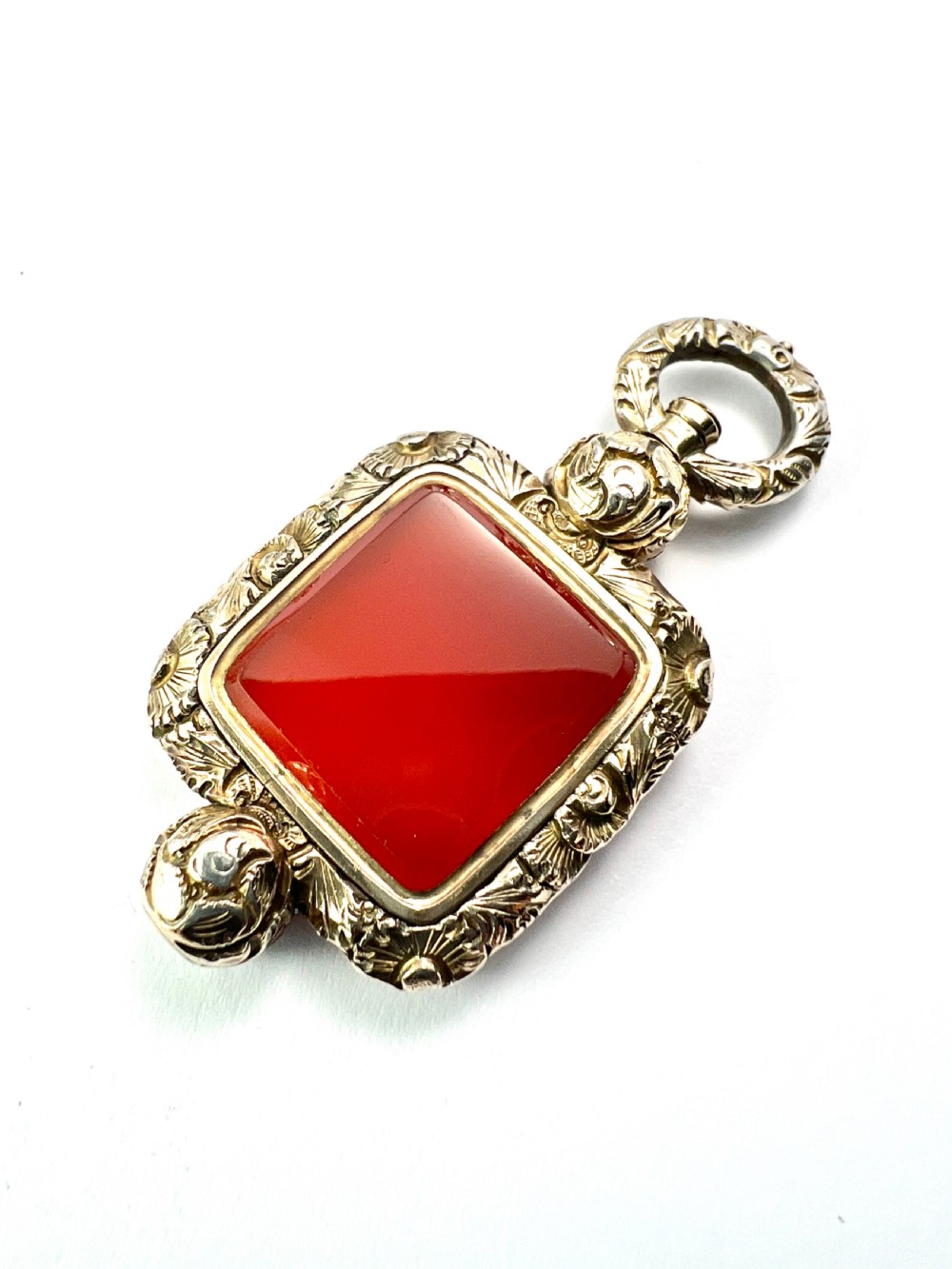 A Georgian era yellow gold watch fob pendant set with a smooth, square red carnelian stone and surrounded by ornate chased scrollwork with a top loop. View III