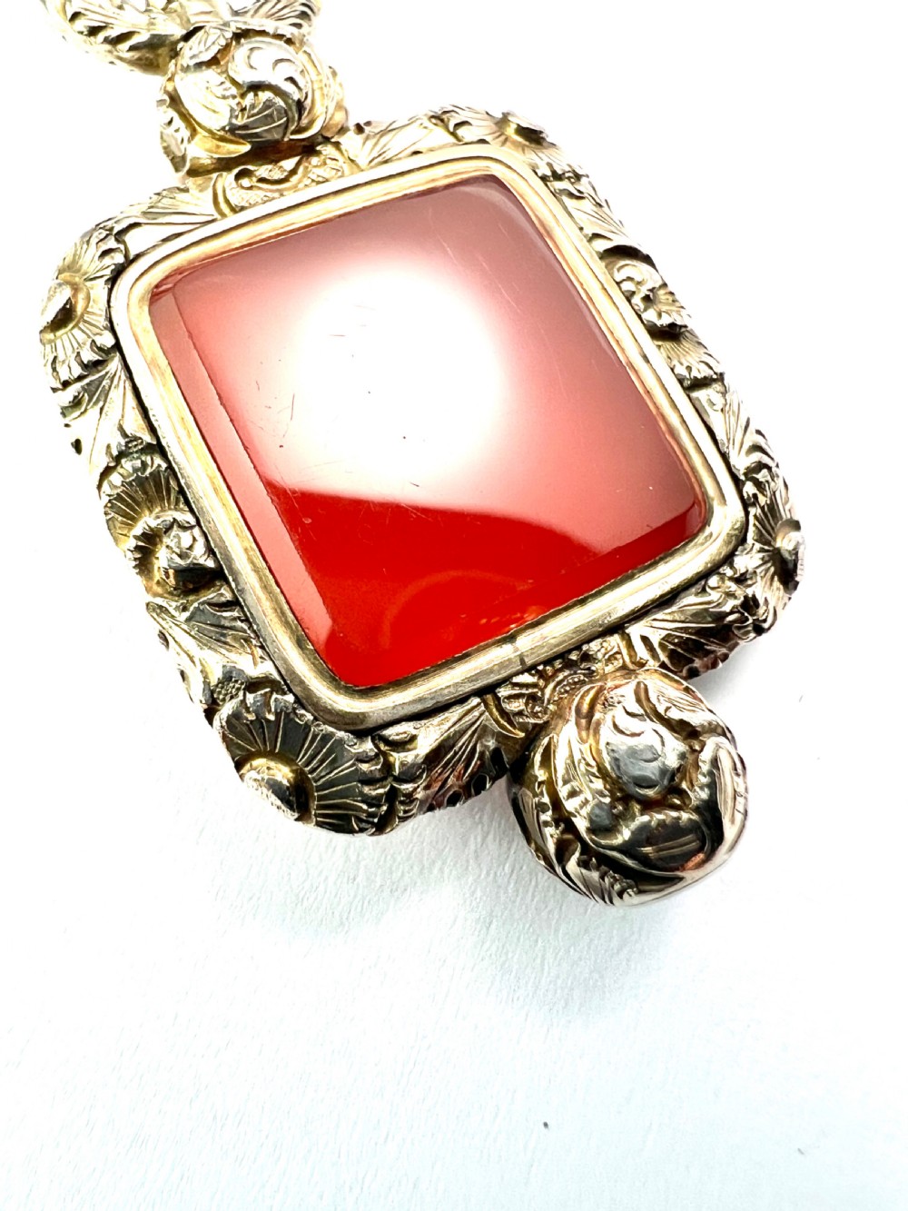 A Georgian era yellow gold watch fob pendant set with a smooth, square red carnelian stone and surrounded by ornate chased scrollwork with a top loop. View IV