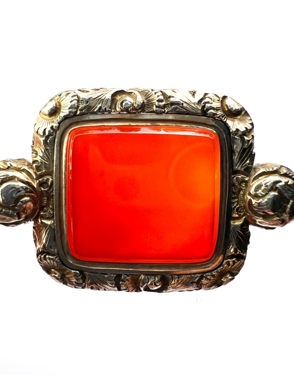 A Georgian era yellow gold watch fob pendant set with a smooth, square red carnelian stone and surrounded by ornate chased scrollwork with a top loop. View V