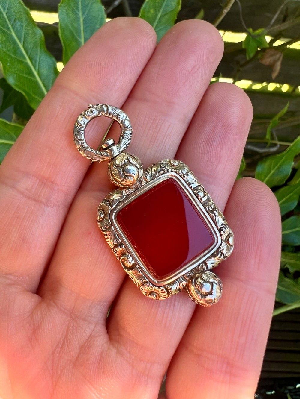 A Georgian era yellow gold watch fob pendant set with a smooth, square red carnelian stone and surrounded by ornate chased scrollwork with a top loop. View VIII