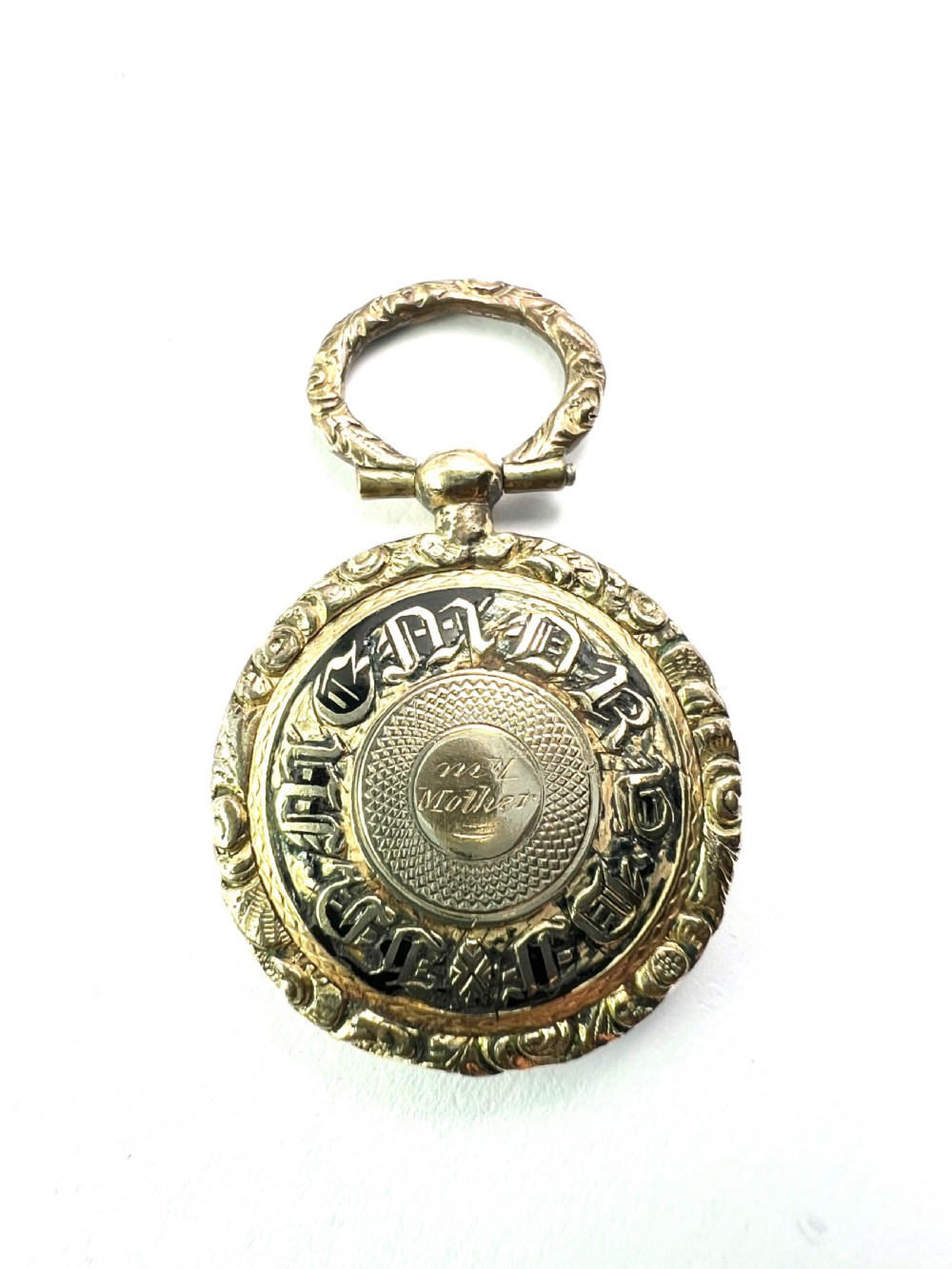 A circular antique gold mourning locket watch fob pendant featuring an intricately engraved foliate border, a textured ring, a glazed central compartment, and a top suspension loop. View IV