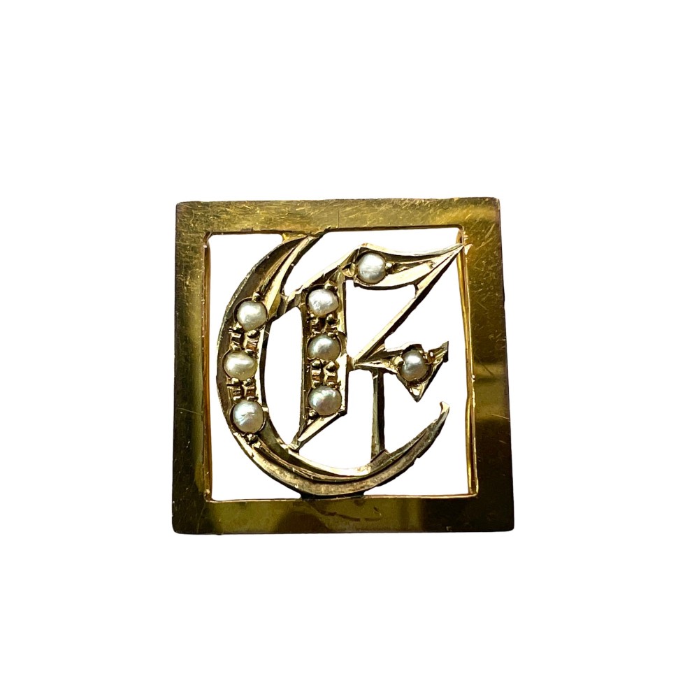 A square 9ct yellow gold Victorian ribbon slider pendant featuring a gothic letter E set with seed pearls.