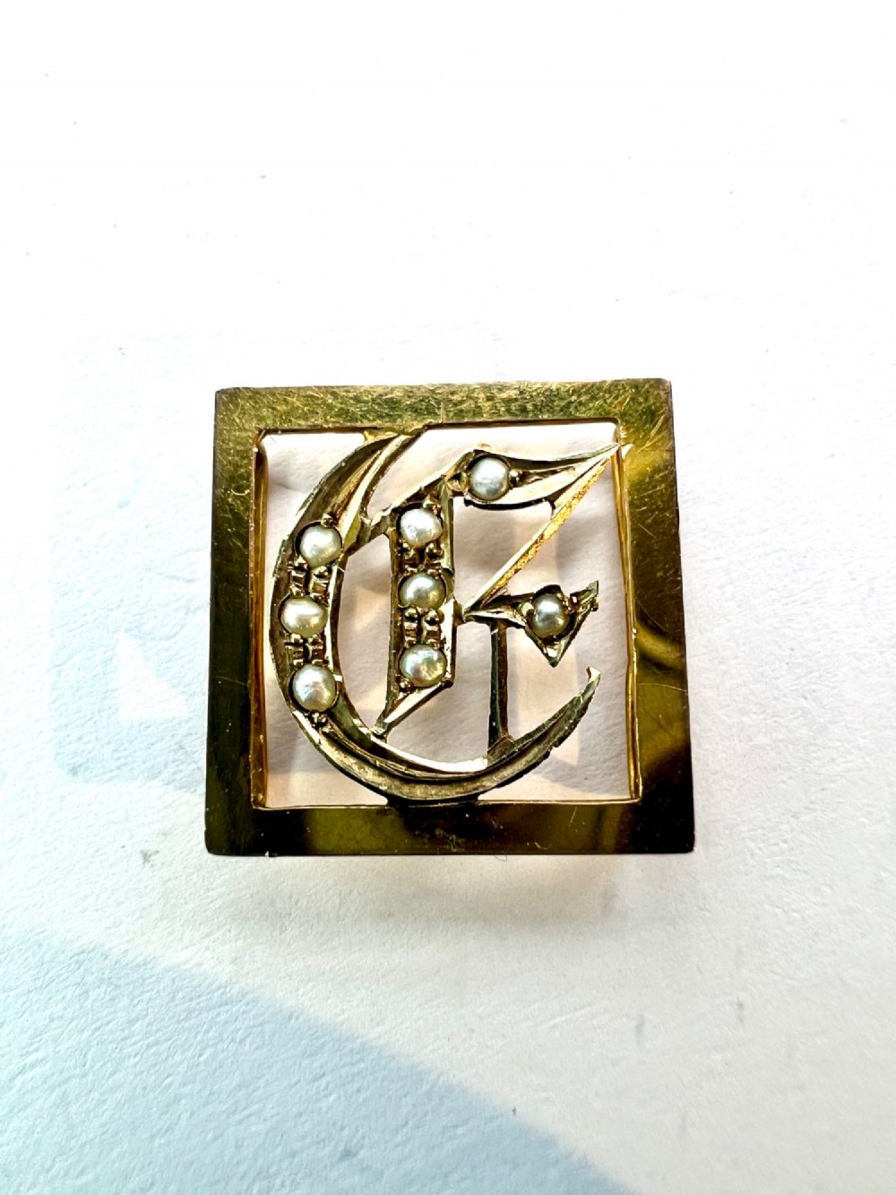 A square 9ct yellow gold Victorian ribbon slider pendant featuring a gothic letter E set with seed pearls. View VI