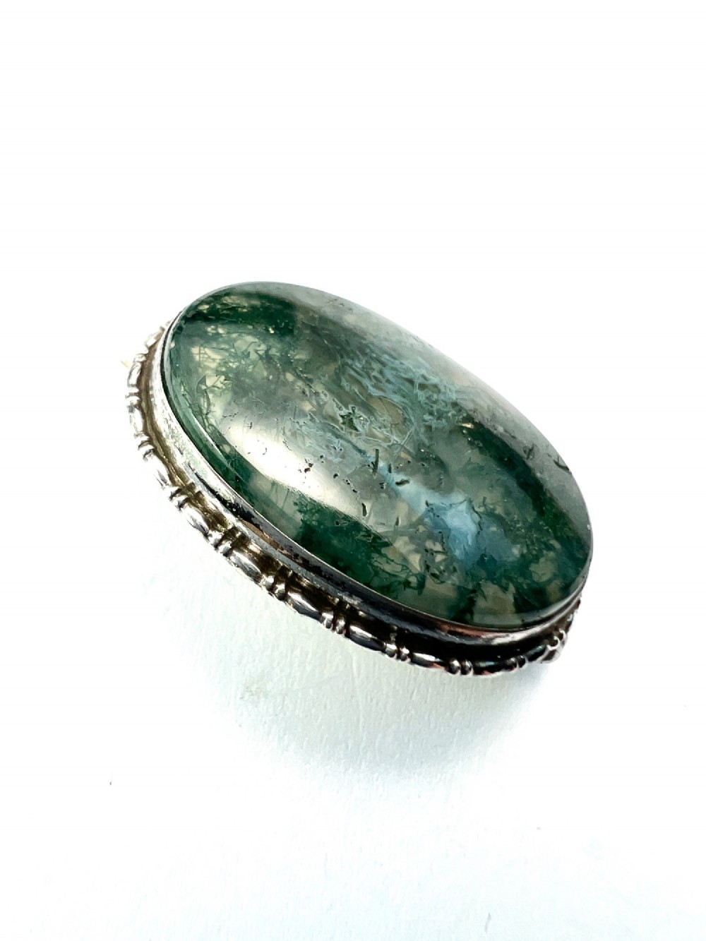 An oval antique sterling silver brooch featuring a translucent moss agate cabochon with green dendritic inclusions within an engraved bezel frame. View IV