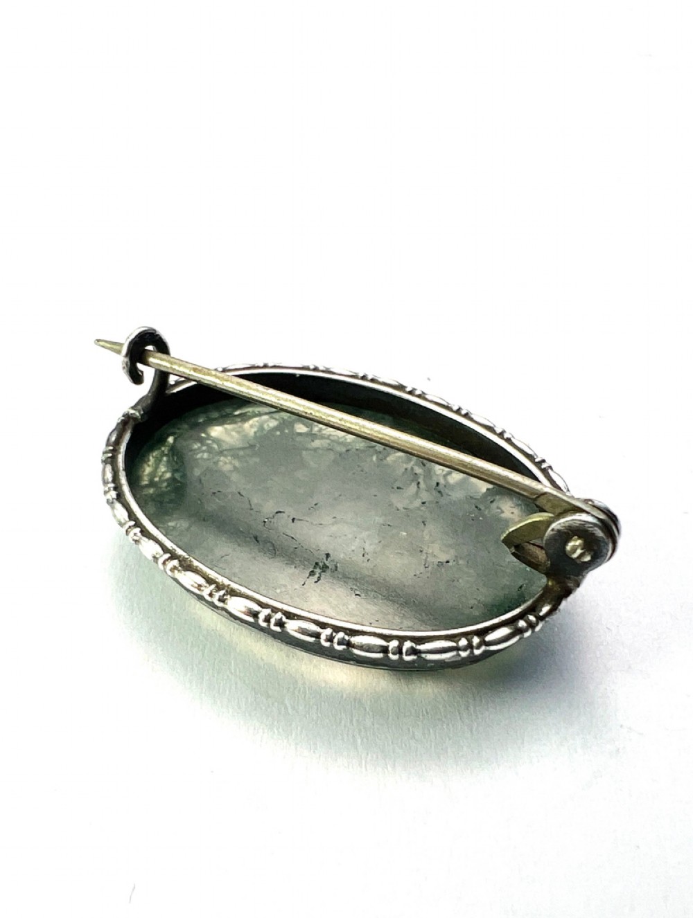 An oval antique sterling silver brooch featuring a translucent moss agate cabochon with green dendritic inclusions within an engraved bezel frame. View VI