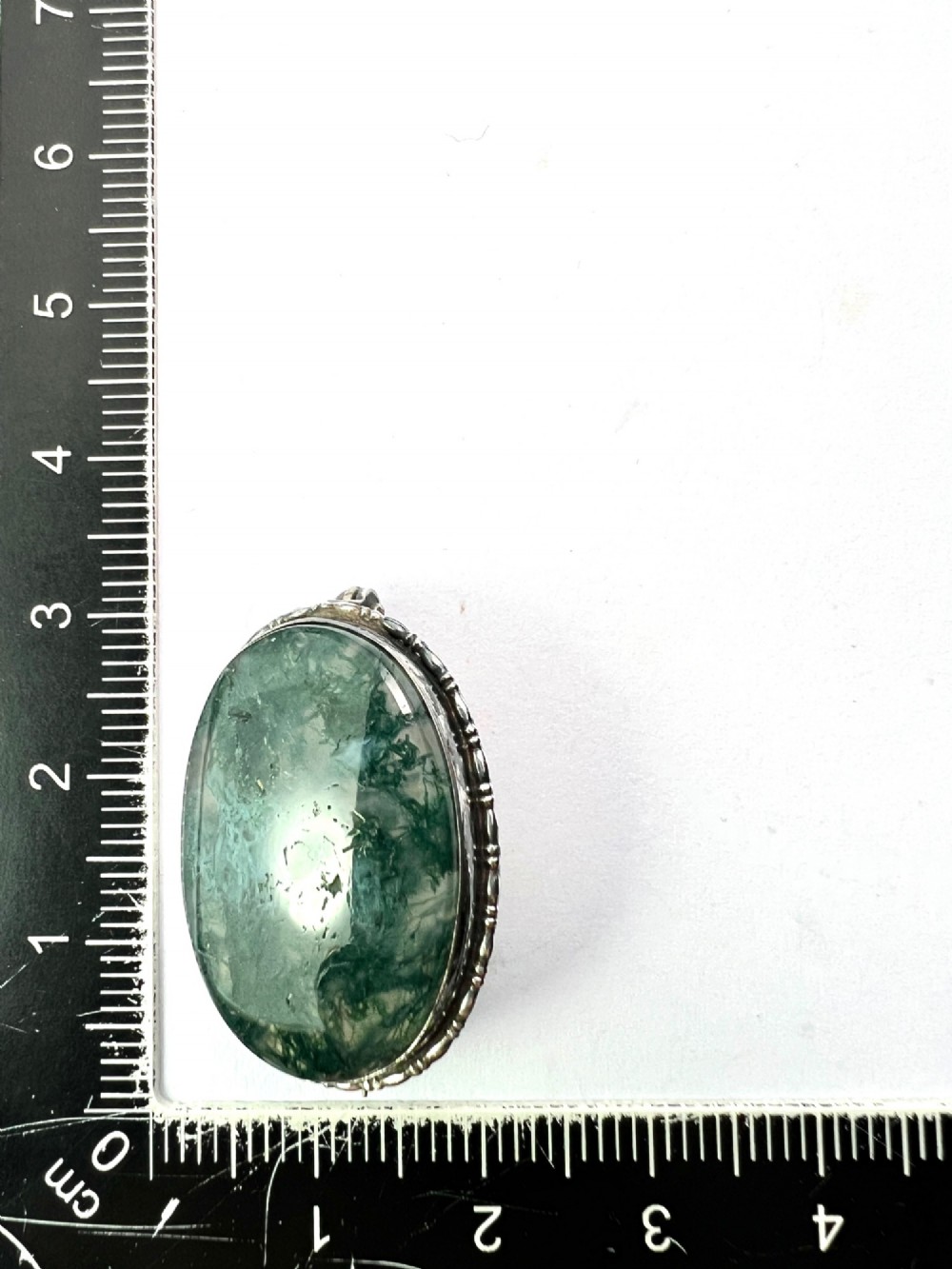 An oval antique sterling silver brooch featuring a translucent moss agate cabochon with green dendritic inclusions within an engraved bezel frame. View VII