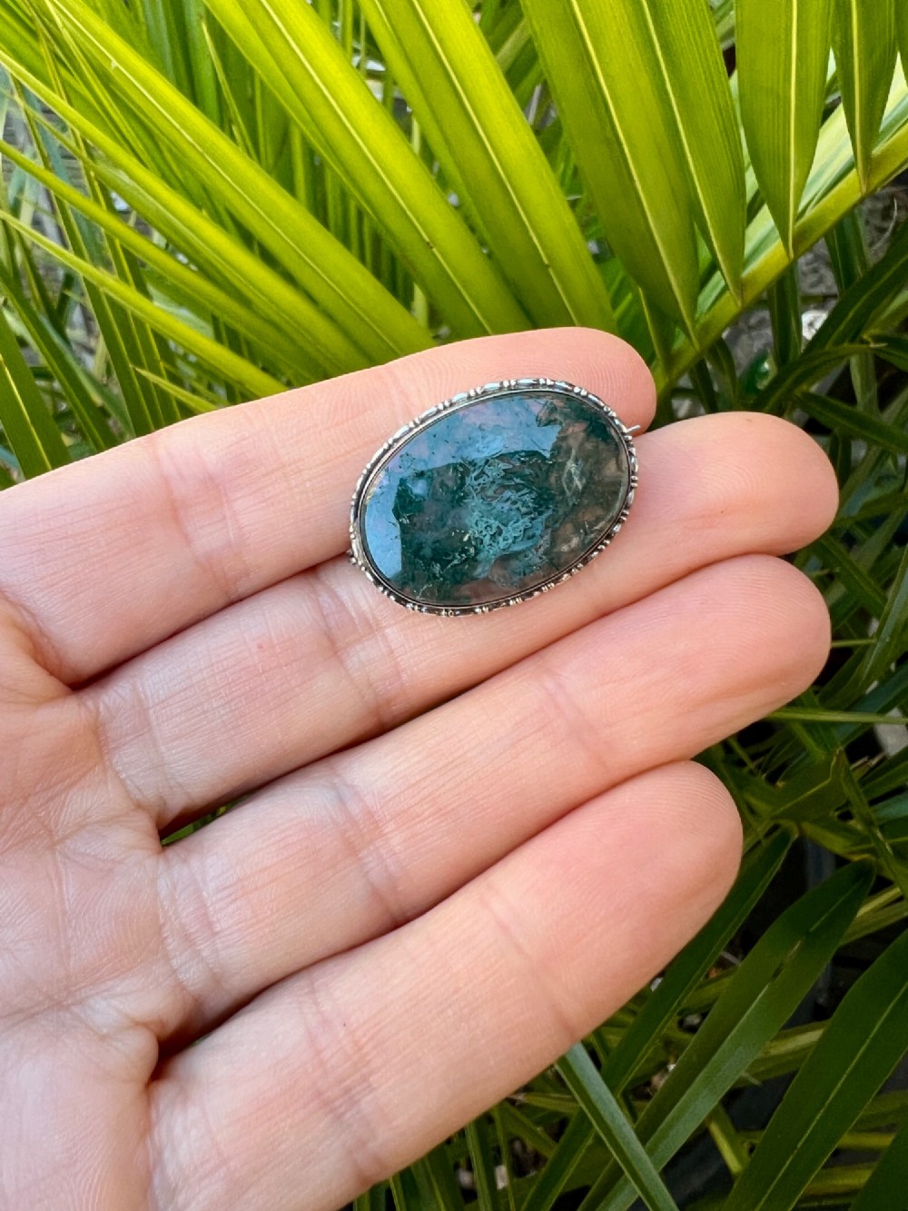 An oval antique sterling silver brooch featuring a translucent moss agate cabochon with green dendritic inclusions within an engraved bezel frame. View VIII