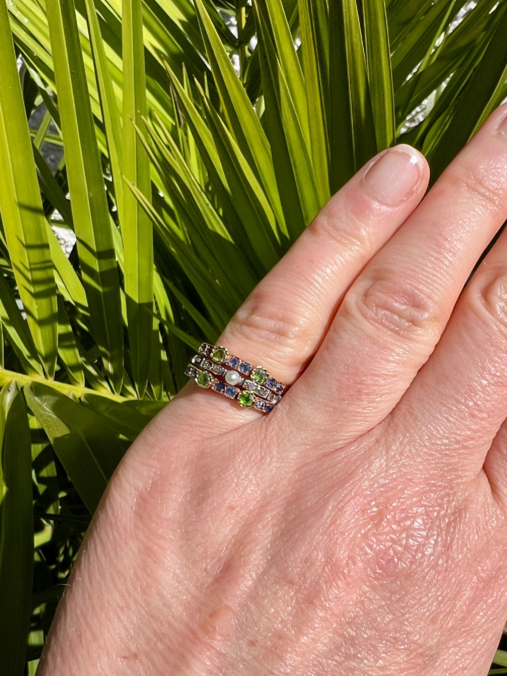 An Edwardian multi-band harem ring crafted in gold and silver, set with green and blue gemstones, diamonds, and a central pearl. View IX