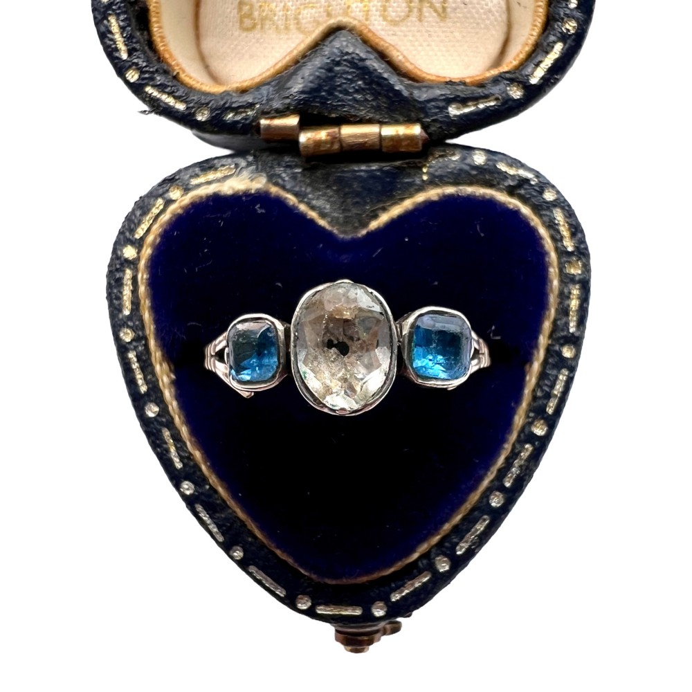 A Georgian three-stone ring featuring a central oval clear paste stone flanked by two blue cushion-cut paste stones set in silver and gold.