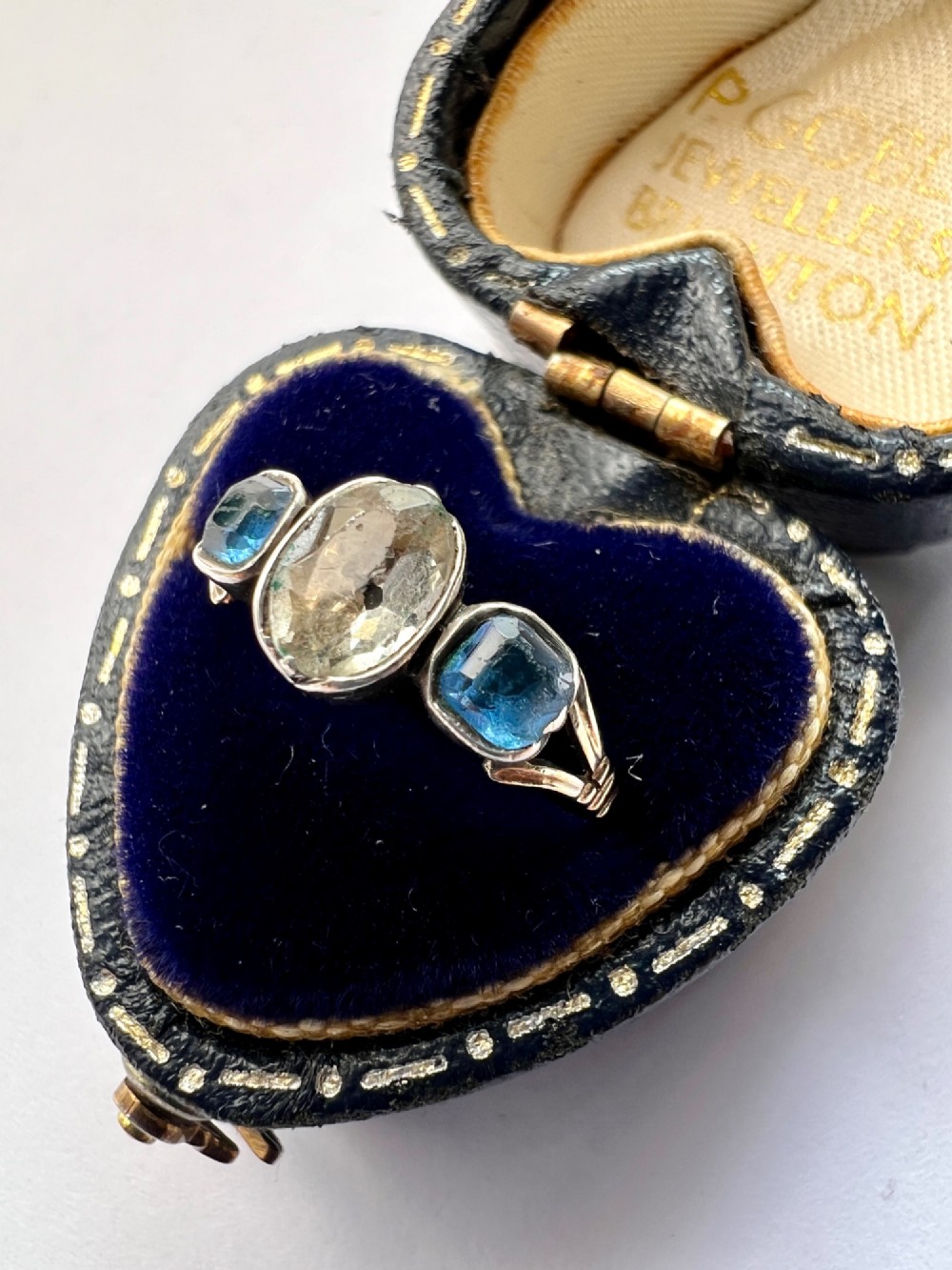 A Georgian three-stone ring featuring a central oval clear paste stone flanked by two blue cushion-cut paste stones set in silver and gold. View III