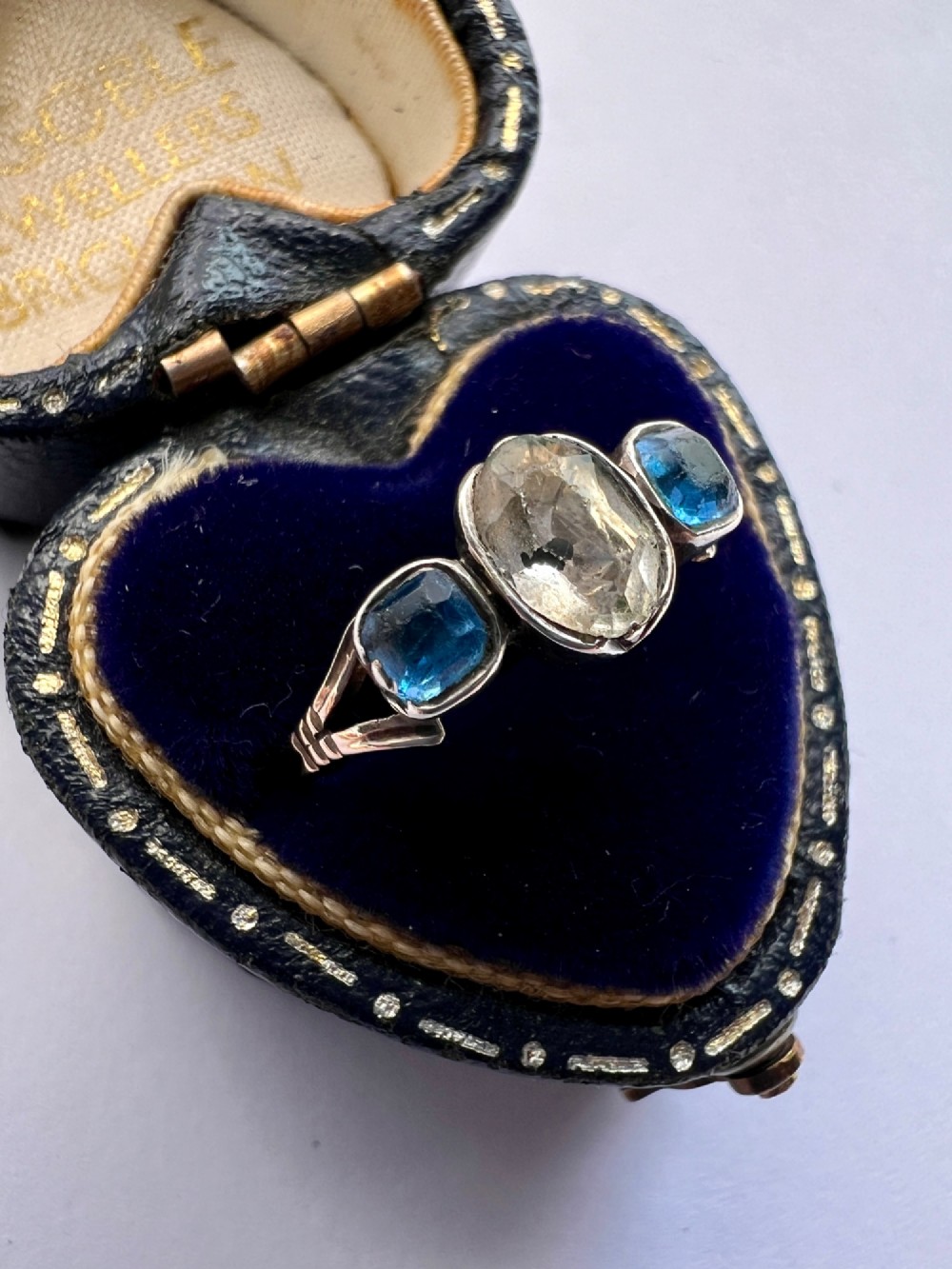 A Georgian three-stone ring featuring a central oval clear paste stone flanked by two blue cushion-cut paste stones set in silver and gold. View IV