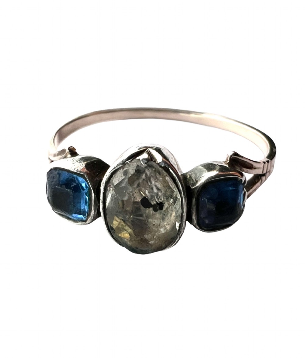 A Georgian three-stone ring featuring a central oval clear paste stone flanked by two blue cushion-cut paste stones set in silver and gold. View V