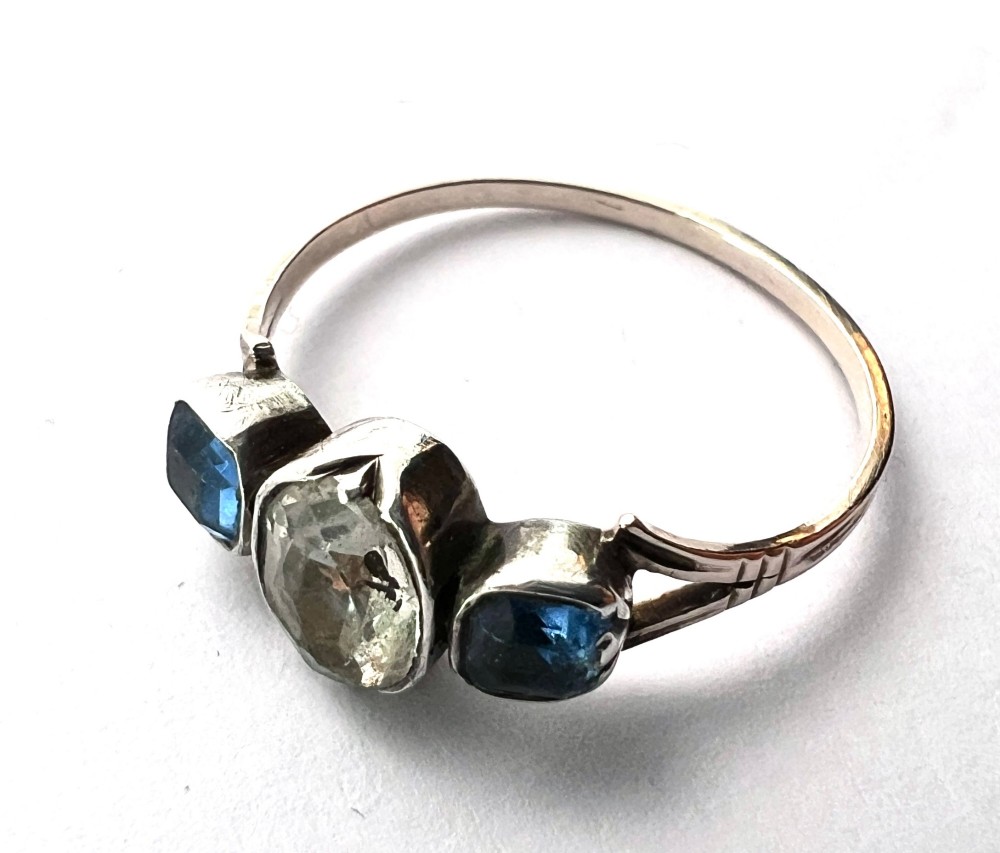 A Georgian three-stone ring featuring a central oval clear paste stone flanked by two blue cushion-cut paste stones set in silver and gold. View VI