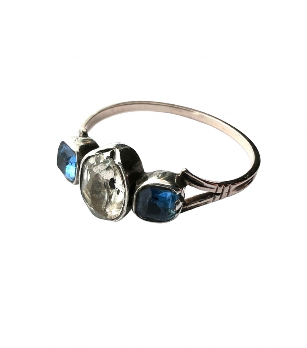 A Georgian three-stone ring featuring a central oval clear paste stone flanked by two blue cushion-cut paste stones set in silver and gold. View VIII