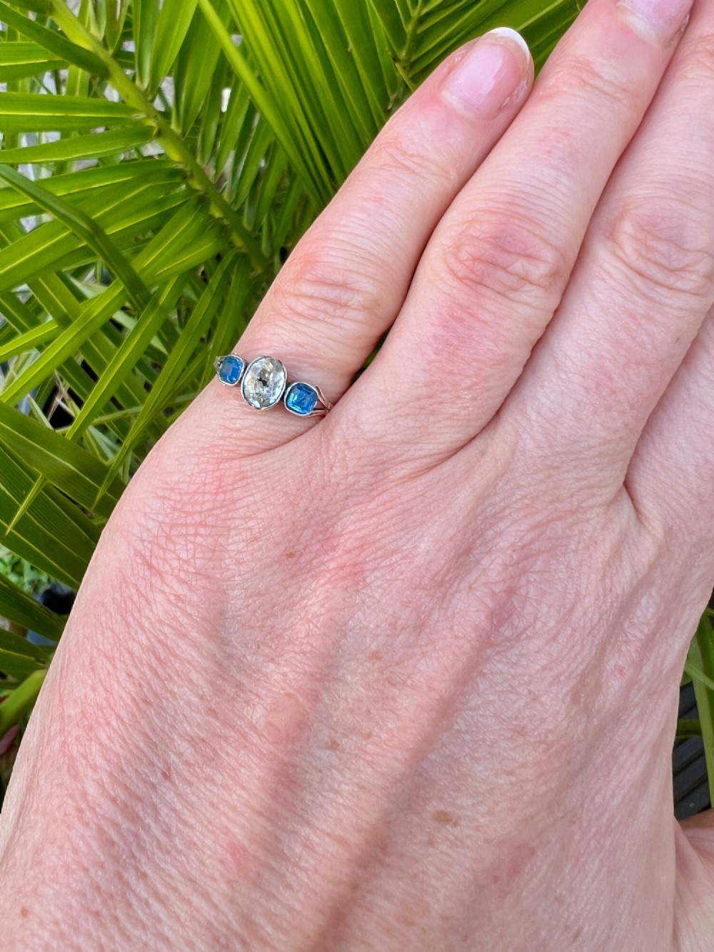 A Georgian three-stone ring featuring a central oval clear paste stone flanked by two blue cushion-cut paste stones set in silver and gold. View IX