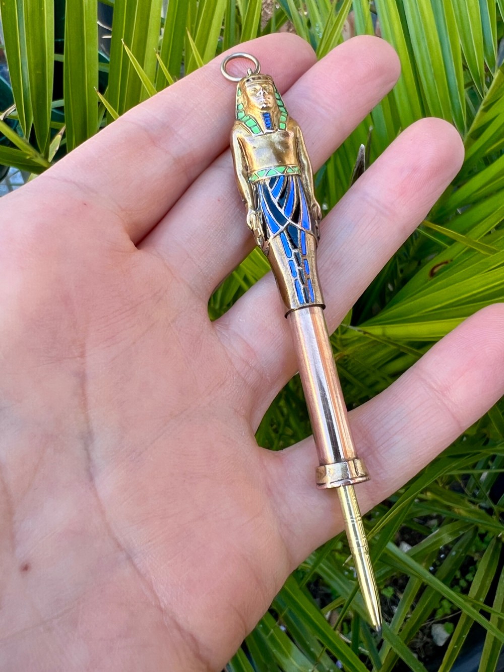 An antique gilt metal and enamel Egyptian Revival sarcophagus pendant featuring a pharaoh figure with blue and green enamelled detailing, designed as a mechanical propelling pencil. View III