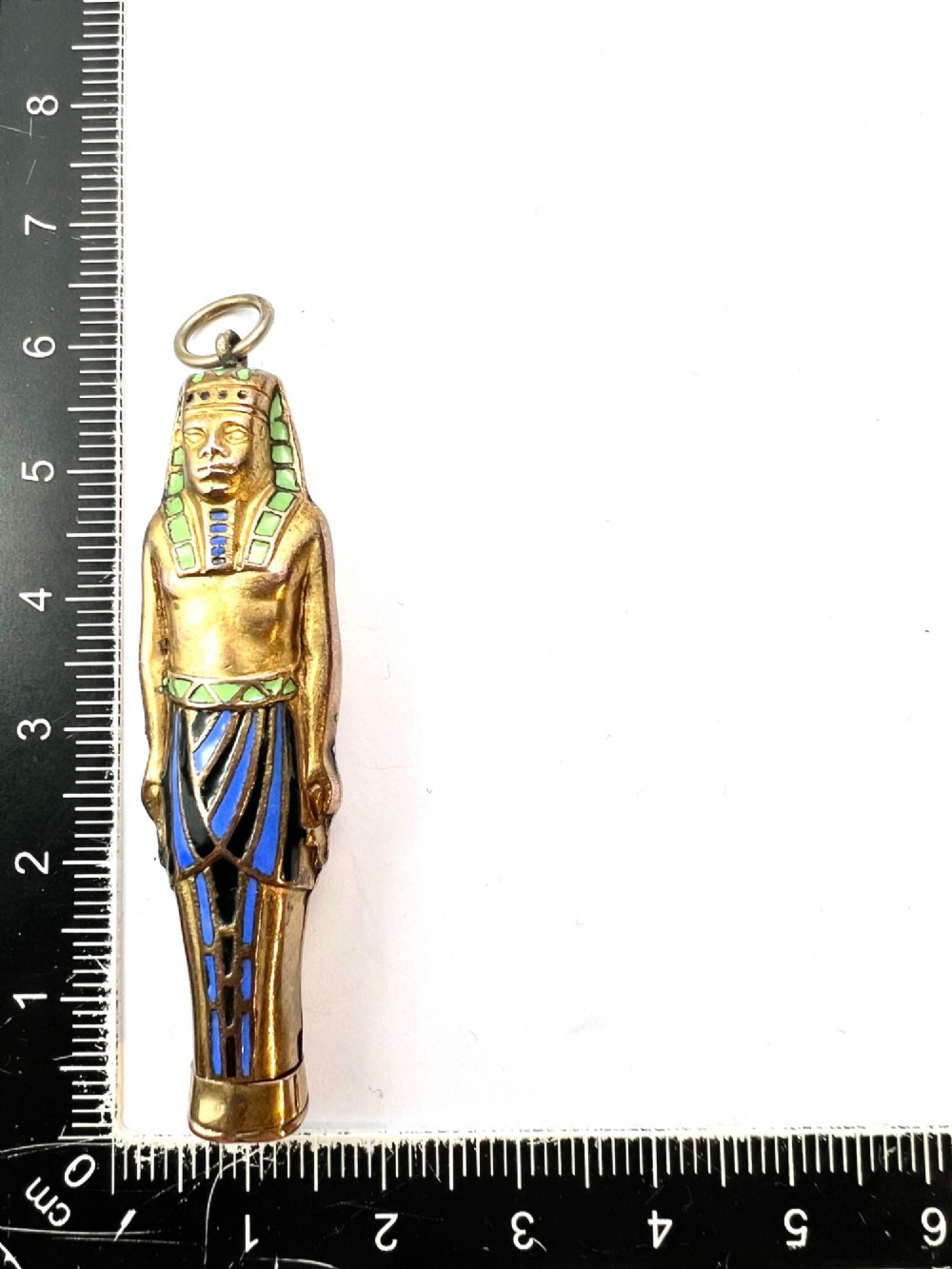 An antique gilt metal and enamel Egyptian Revival sarcophagus pendant featuring a pharaoh figure with blue and green enamelled detailing, designed as a mechanical propelling pencil. View X