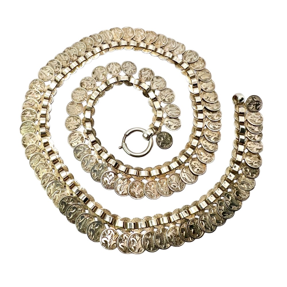 A coiled Victorian sterling silver chain decorated with overlapping, hand-engraved circular coin discs and secured with a traditional bolt ring clasp.