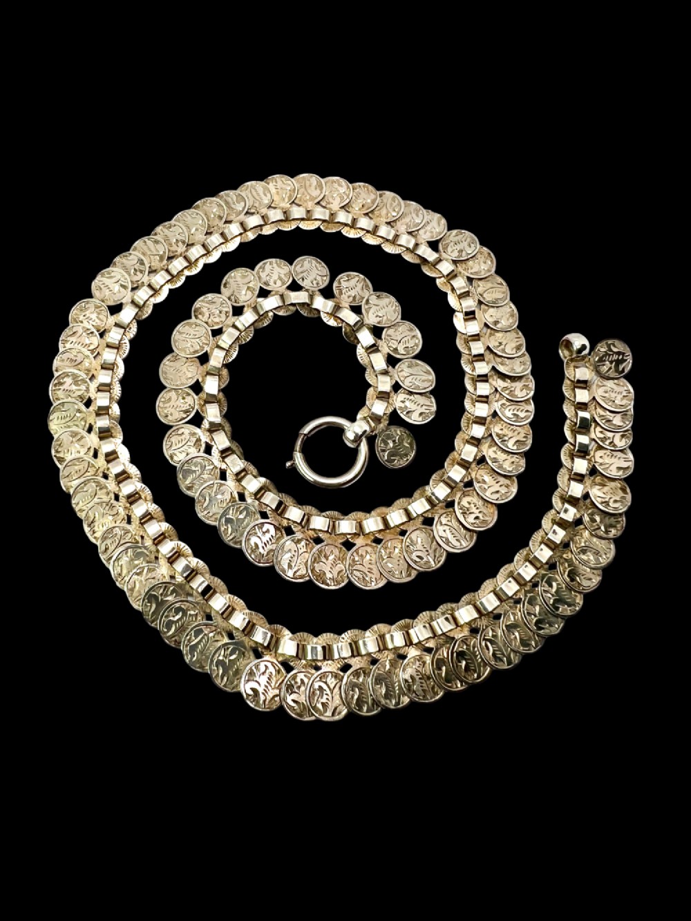 A coiled Victorian sterling silver chain decorated with overlapping, hand-engraved circular coin discs and secured with a traditional bolt ring clasp. View II