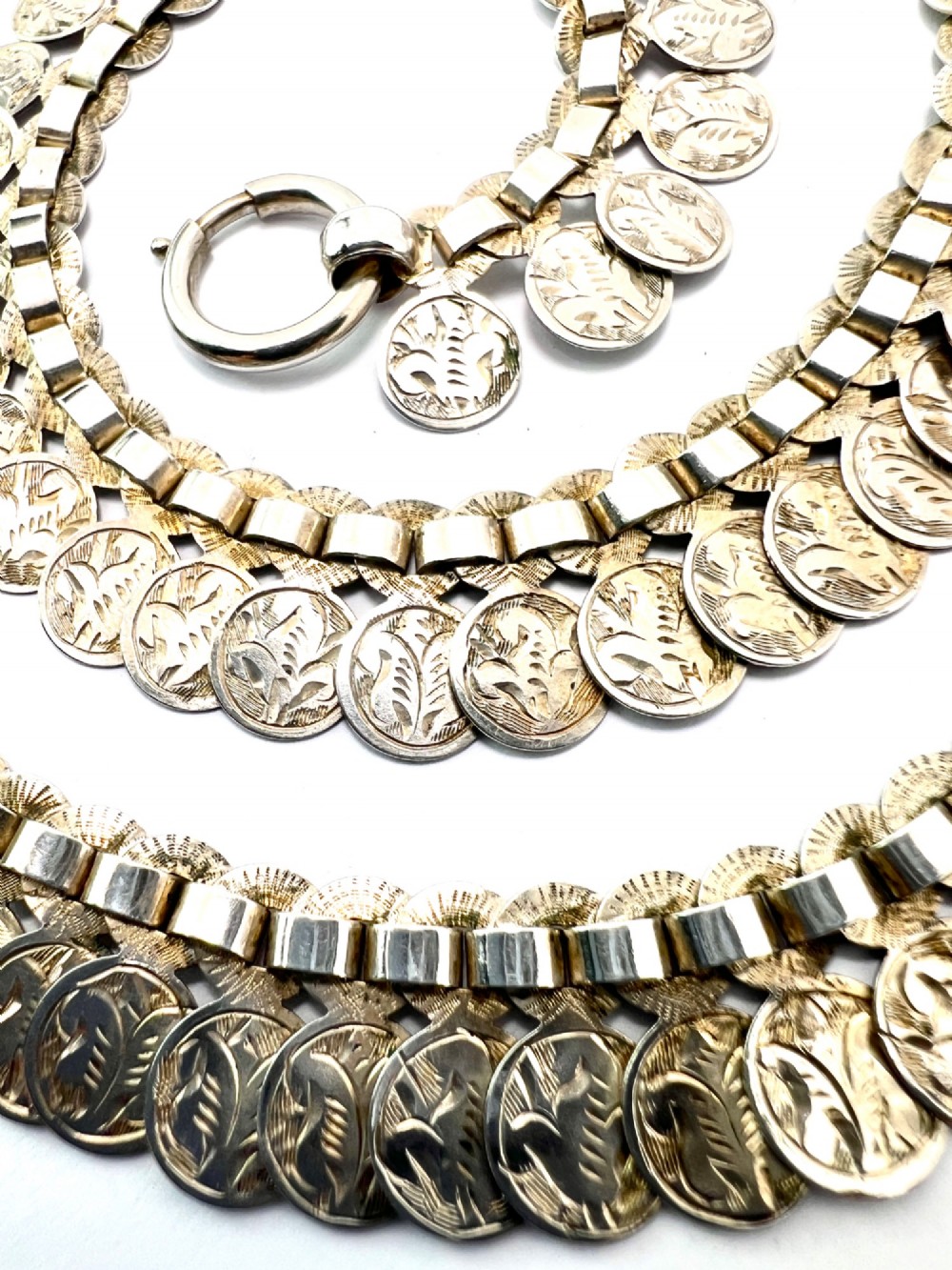 A coiled Victorian sterling silver chain decorated with overlapping, hand-engraved circular coin discs and secured with a traditional bolt ring clasp. View III