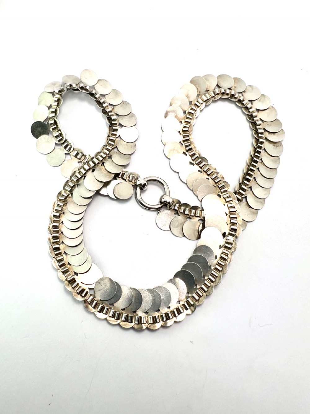 A coiled Victorian sterling silver chain decorated with overlapping, hand-engraved circular coin discs and secured with a traditional bolt ring clasp. View V