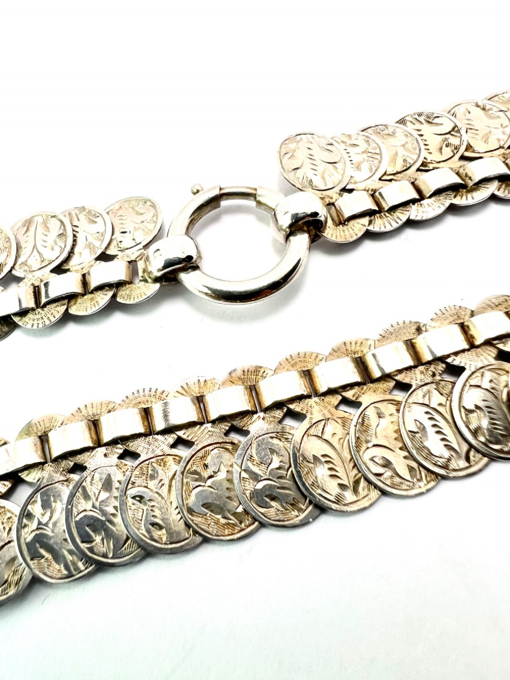 A coiled Victorian sterling silver chain decorated with overlapping, hand-engraved circular coin discs and secured with a traditional bolt ring clasp. View VI