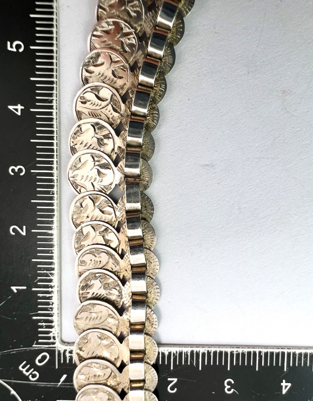 A coiled Victorian sterling silver chain decorated with overlapping, hand-engraved circular coin discs and secured with a traditional bolt ring clasp. View VII