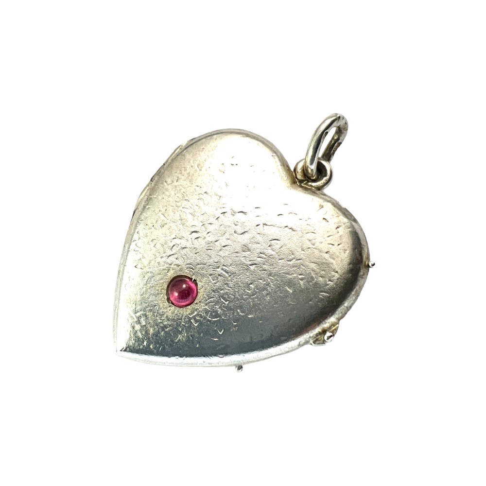 A textured silver heart-shaped locket pendant with a flush-set red cabochon stone and a top bail ring.