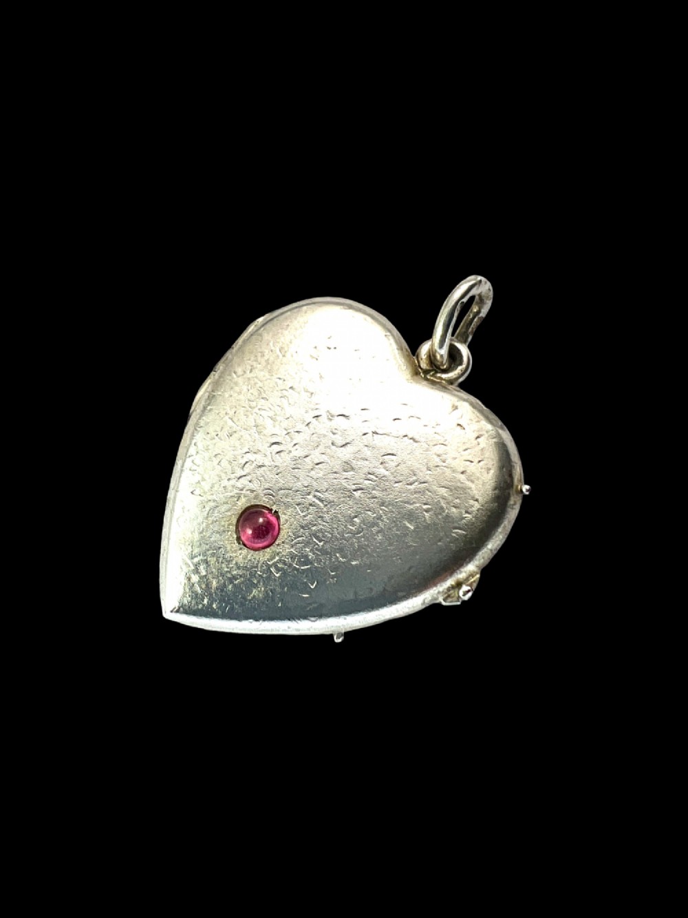 A textured silver heart-shaped locket pendant with a flush-set red cabochon stone and a top bail ring. View II