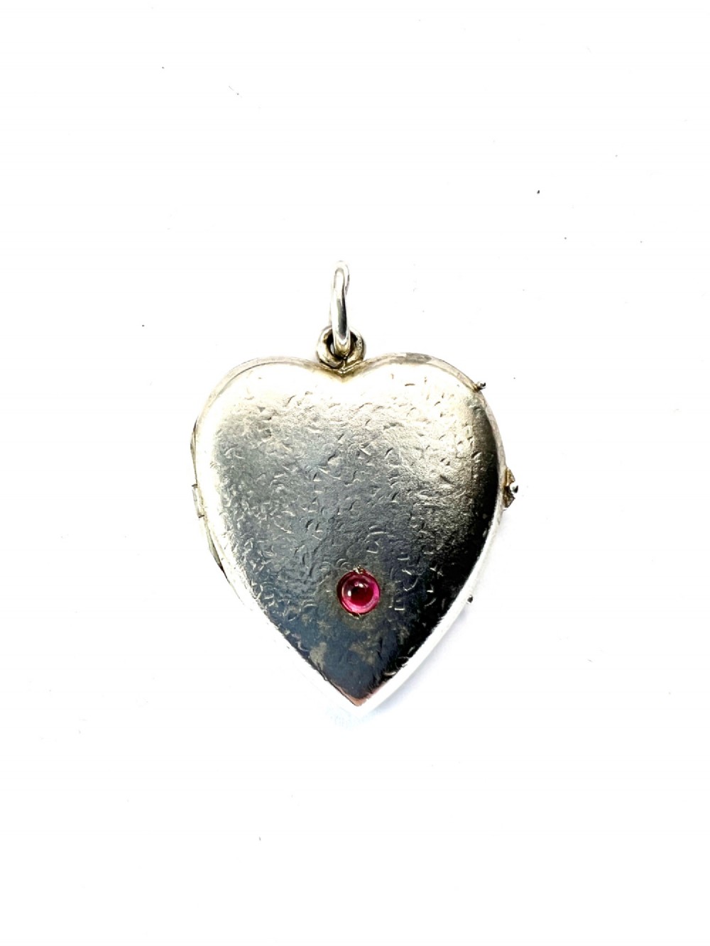A textured silver heart-shaped locket pendant with a flush-set red cabochon stone and a top bail ring. View III
