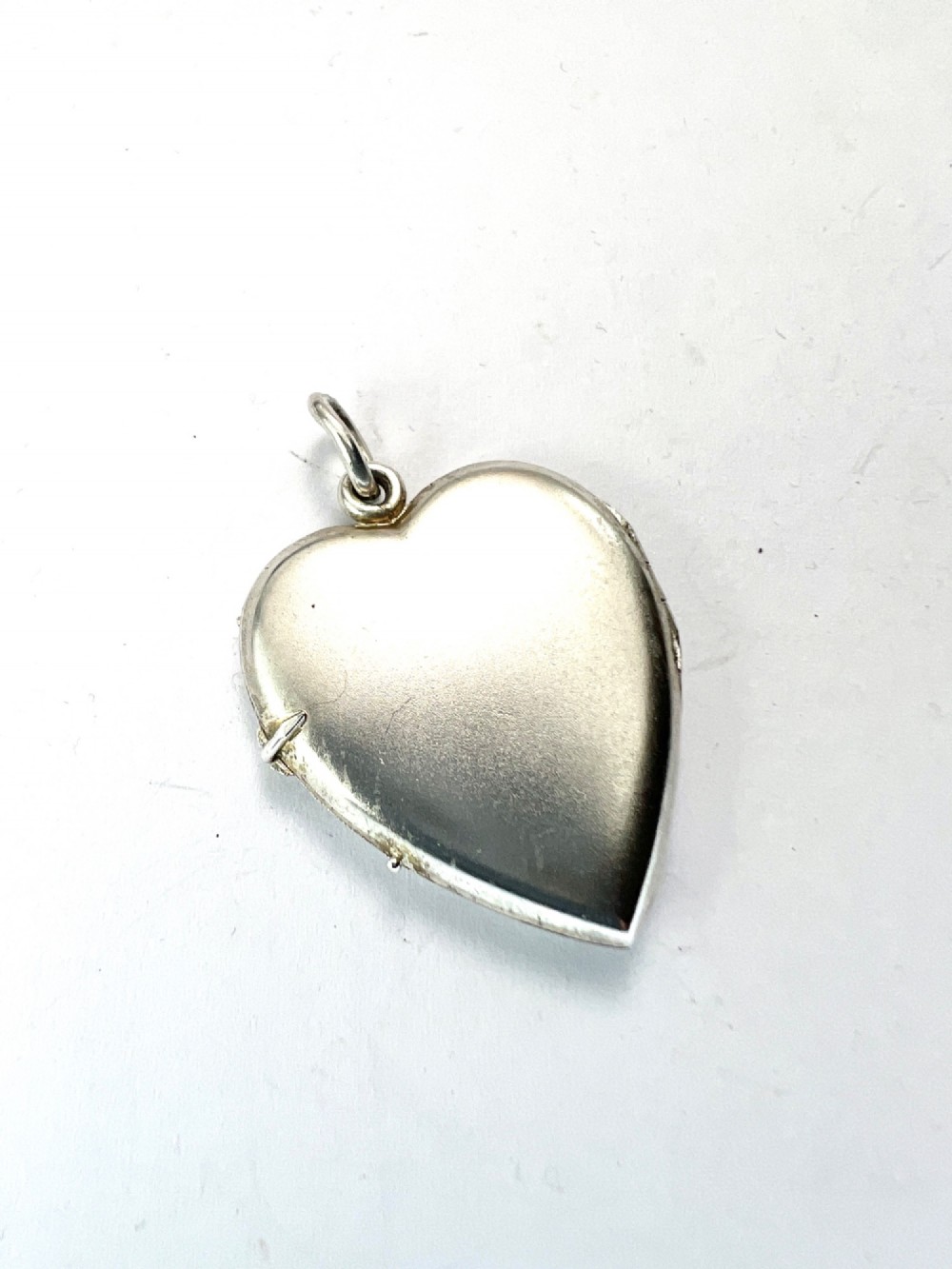A textured silver heart-shaped locket pendant with a flush-set red cabochon stone and a top bail ring. View IV