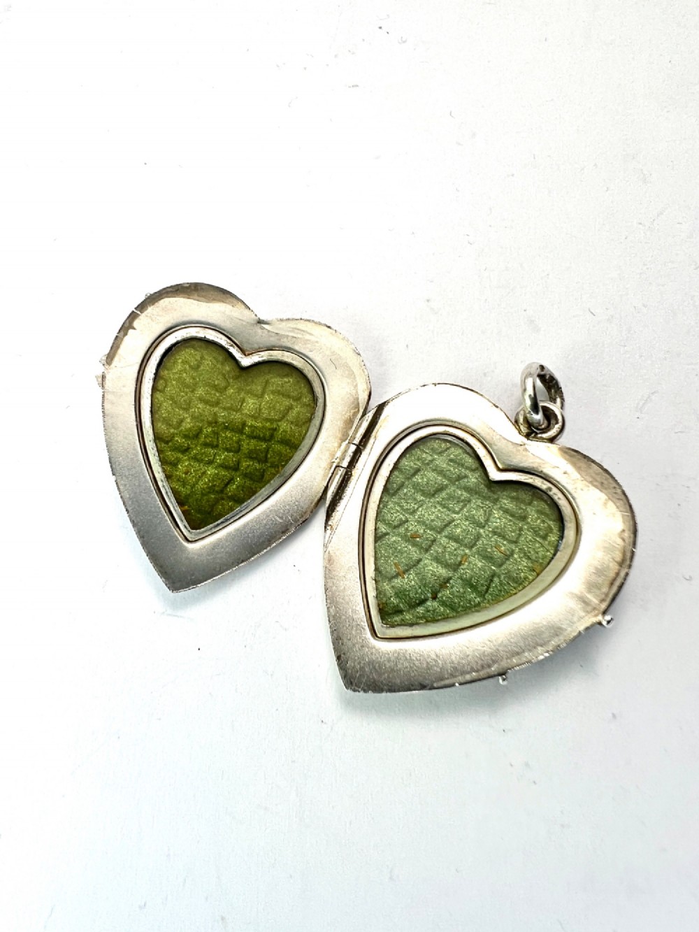 A textured silver heart-shaped locket pendant with a flush-set red cabochon stone and a top bail ring. View V