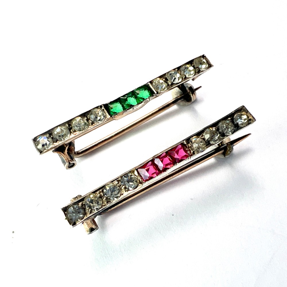 A pair of small rectangular Art Deco bar brooches set with clear paste glass stones featuring central rows of square-cut emerald-green and ruby-red paste gems.