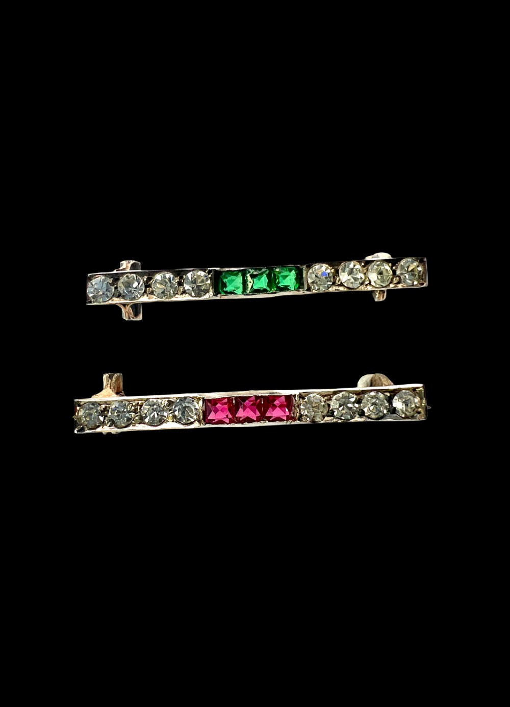 A pair of small rectangular Art Deco bar brooches set with clear paste glass stones featuring central rows of square-cut emerald-green and ruby-red paste gems. View II