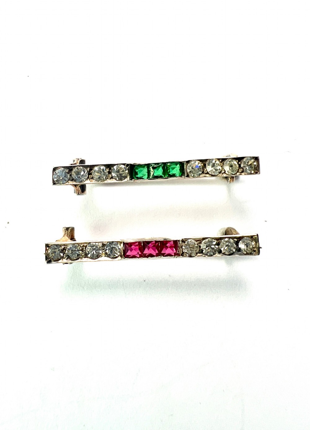 A pair of small rectangular Art Deco bar brooches set with clear paste glass stones featuring central rows of square-cut emerald-green and ruby-red paste gems. View III