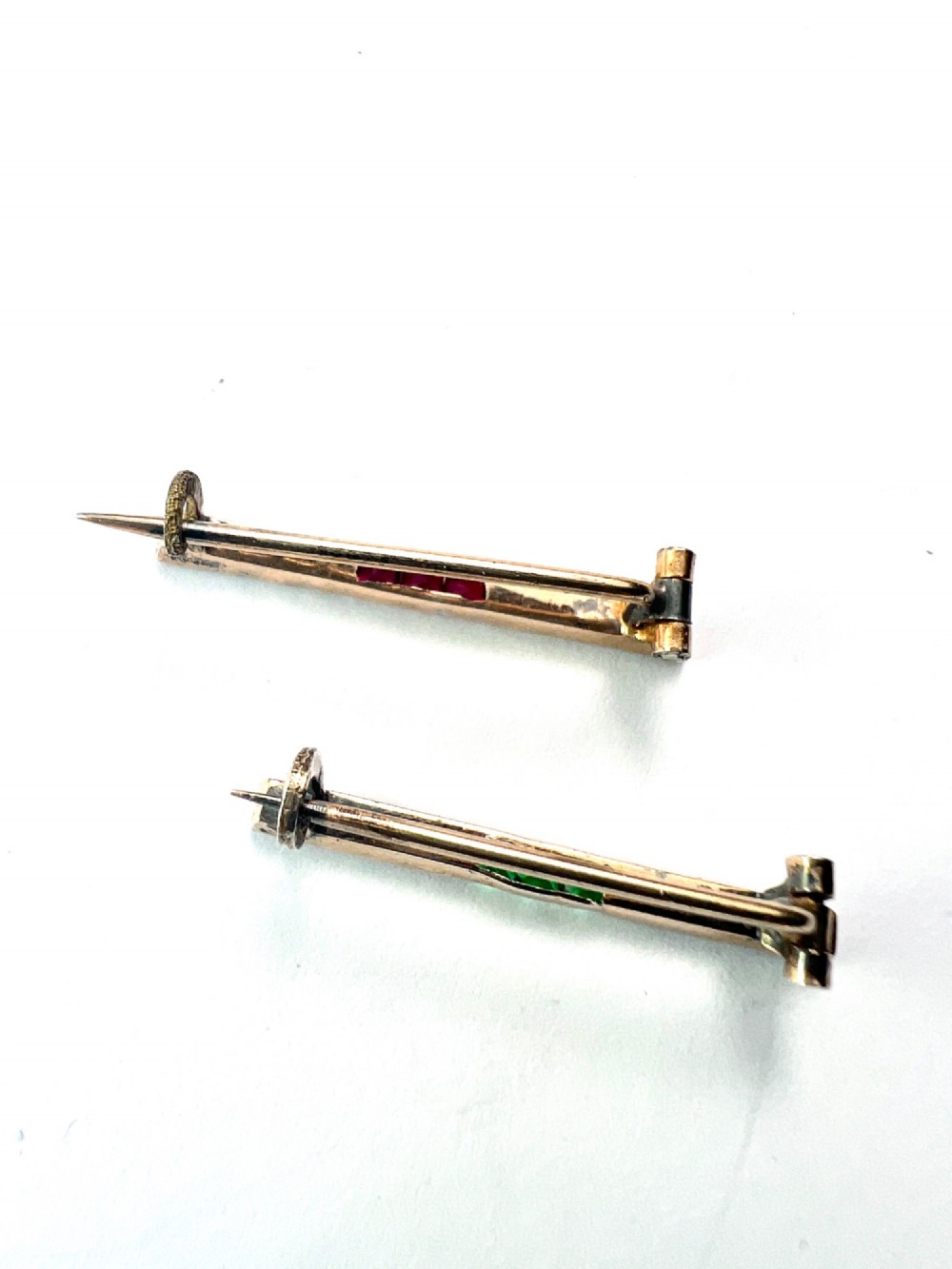 A pair of small rectangular Art Deco bar brooches set with clear paste glass stones featuring central rows of square-cut emerald-green and ruby-red paste gems. View IV