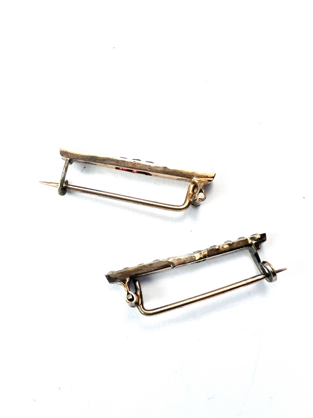 A pair of small rectangular Art Deco bar brooches set with clear paste glass stones featuring central rows of square-cut emerald-green and ruby-red paste gems. View V