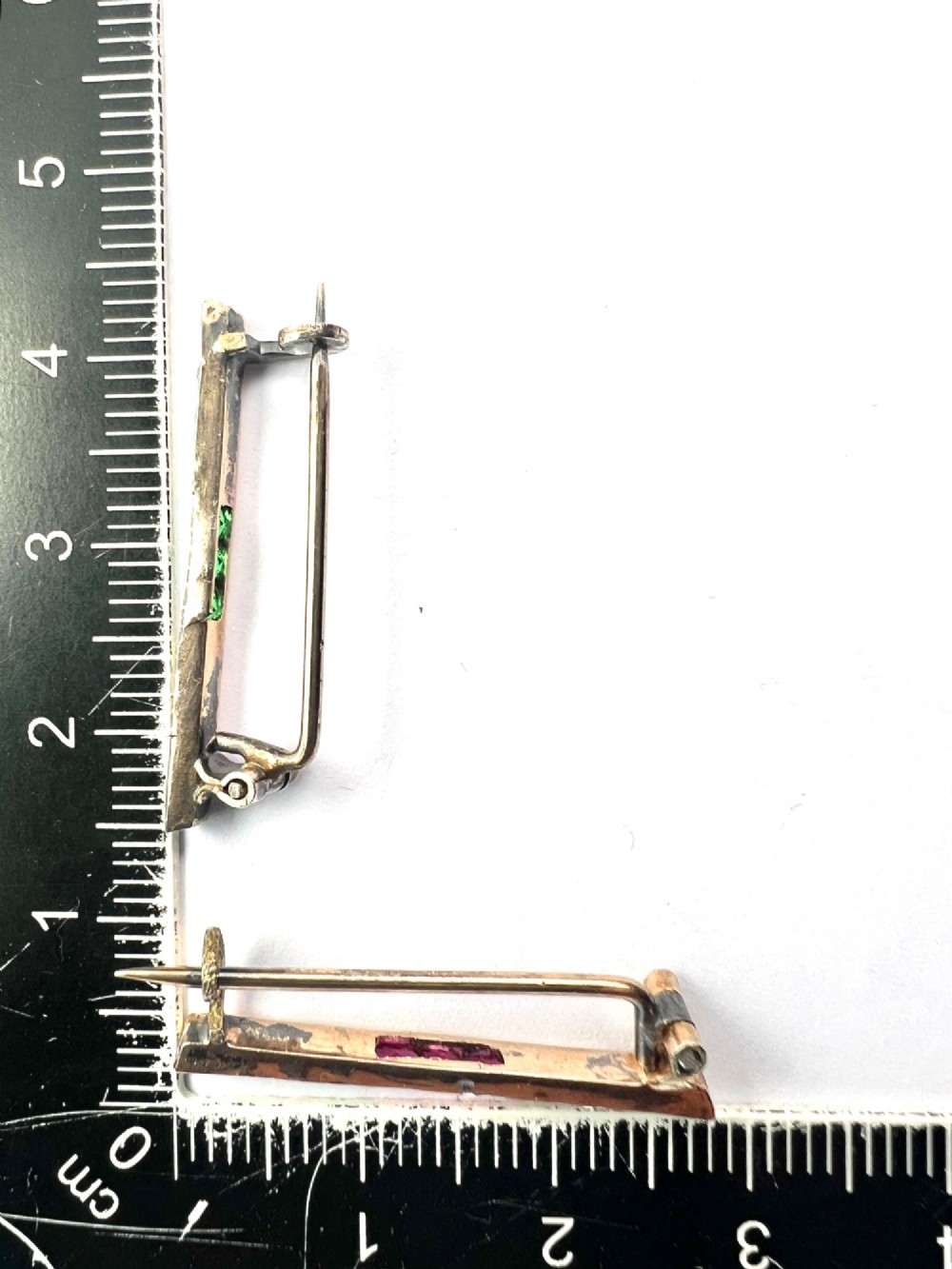 A pair of small rectangular Art Deco bar brooches set with clear paste glass stones featuring central rows of square-cut emerald-green and ruby-red paste gems. View VI