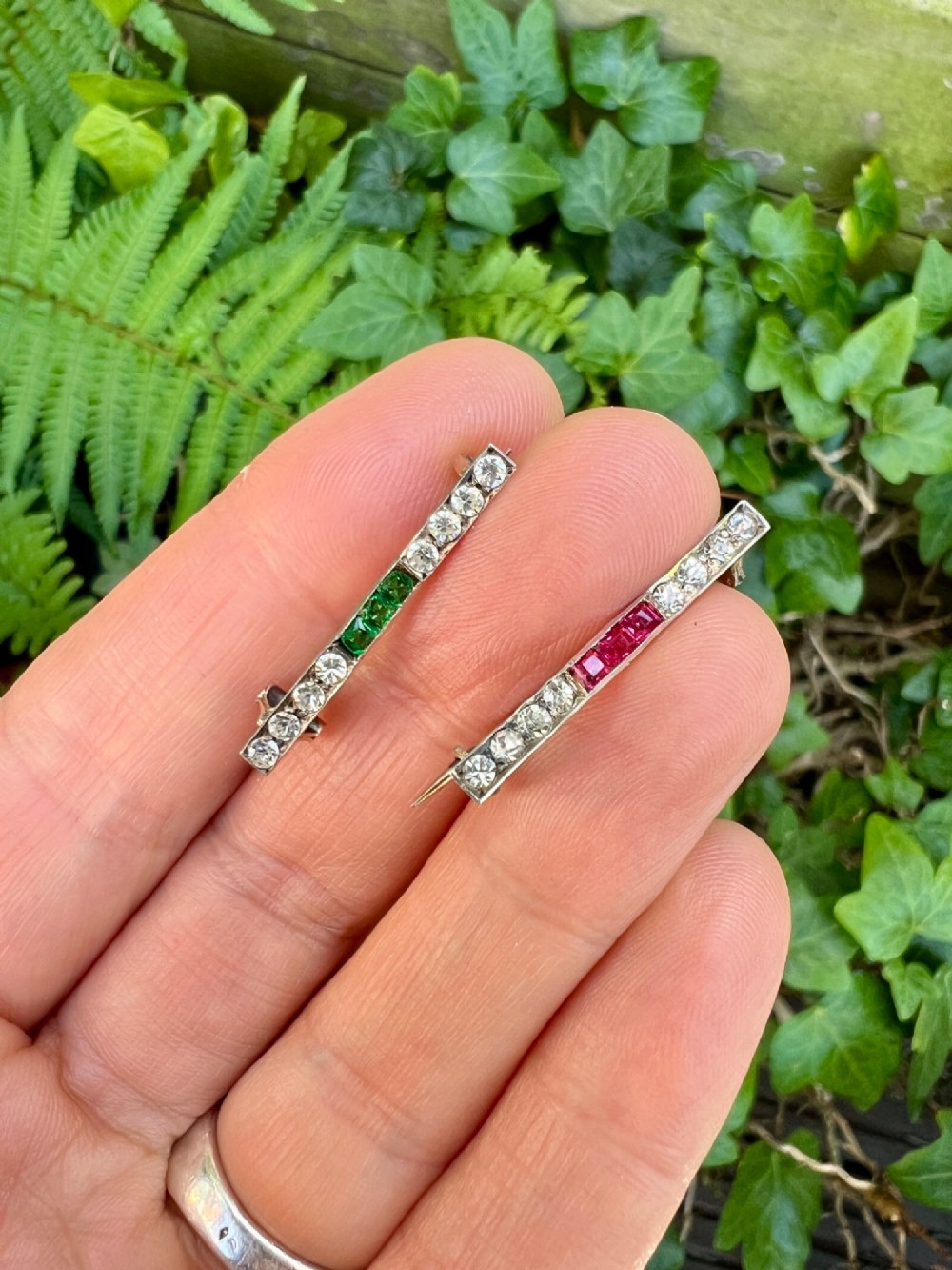 A pair of small rectangular Art Deco bar brooches set with clear paste glass stones featuring central rows of square-cut emerald-green and ruby-red paste gems. View VII