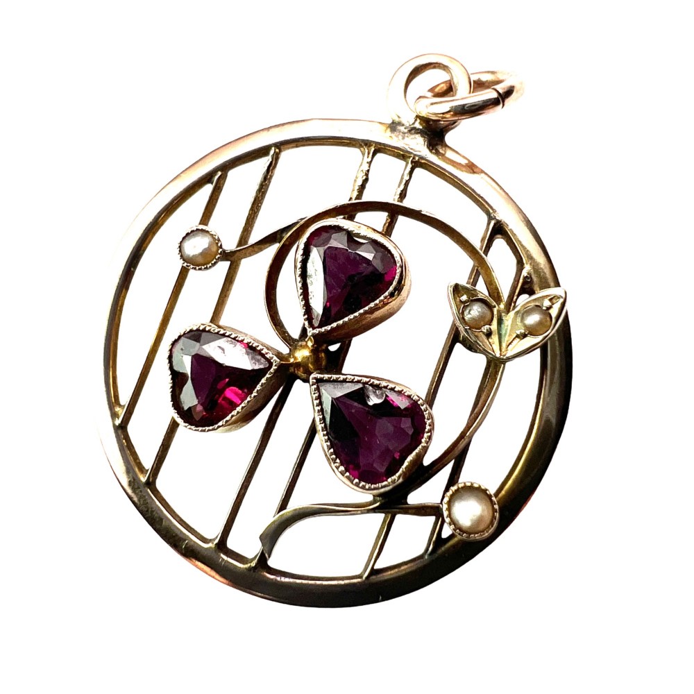 A circular 9ct gold Edwardian openwork pendant featuring three heart-cut deep red garnets forming a clover motif flanked by seed pearls.