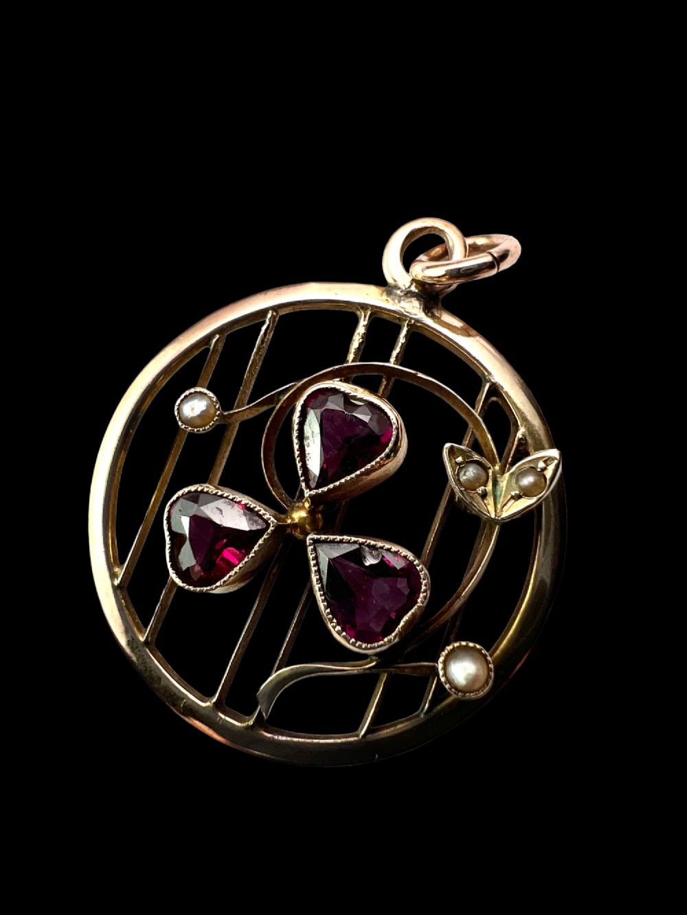 A circular 9ct gold Edwardian openwork pendant featuring three heart-cut deep red garnets forming a clover motif flanked by seed pearls. View II