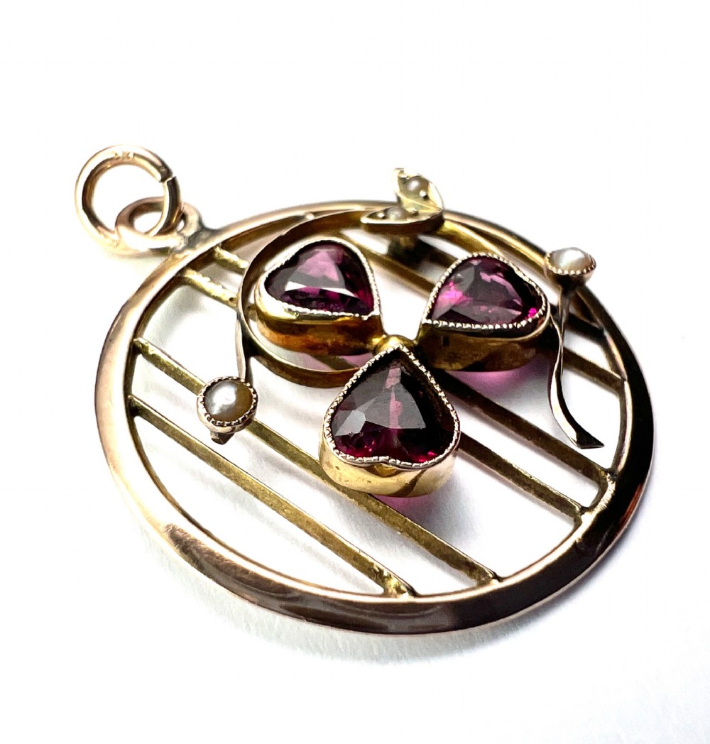 A circular 9ct gold Edwardian openwork pendant featuring three heart-cut deep red garnets forming a clover motif flanked by seed pearls. View III