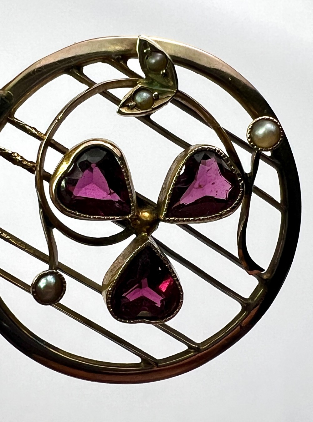 A circular 9ct gold Edwardian openwork pendant featuring three heart-cut deep red garnets forming a clover motif flanked by seed pearls. View IV